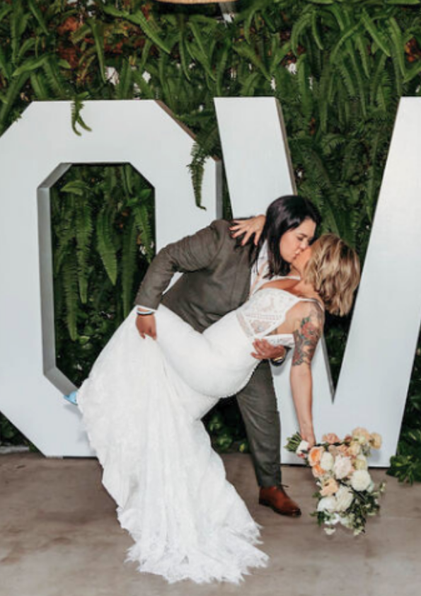 LGBTQ couple kissing in front of the LOVE sign at FruitCraft’s event venue.